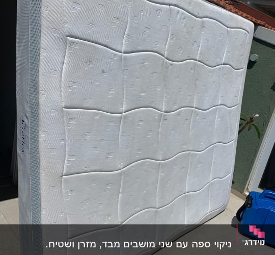 מזרן לבן עומד בחוץ ליד קיר ירוק